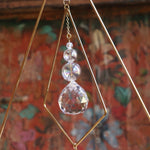 Someone holding the Prisma Tabletop #4 Diamond Tree Brass Suncatcher in front of a wooden background.