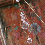 Someone holding the Prisma Tabletop #4 Diamond Tree Brass Suncatcher in front of a wooden background.