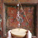 Someone holding the Prisma Tabletop #4 Diamond Tree Brass Suncatcher in front of a wooden background.