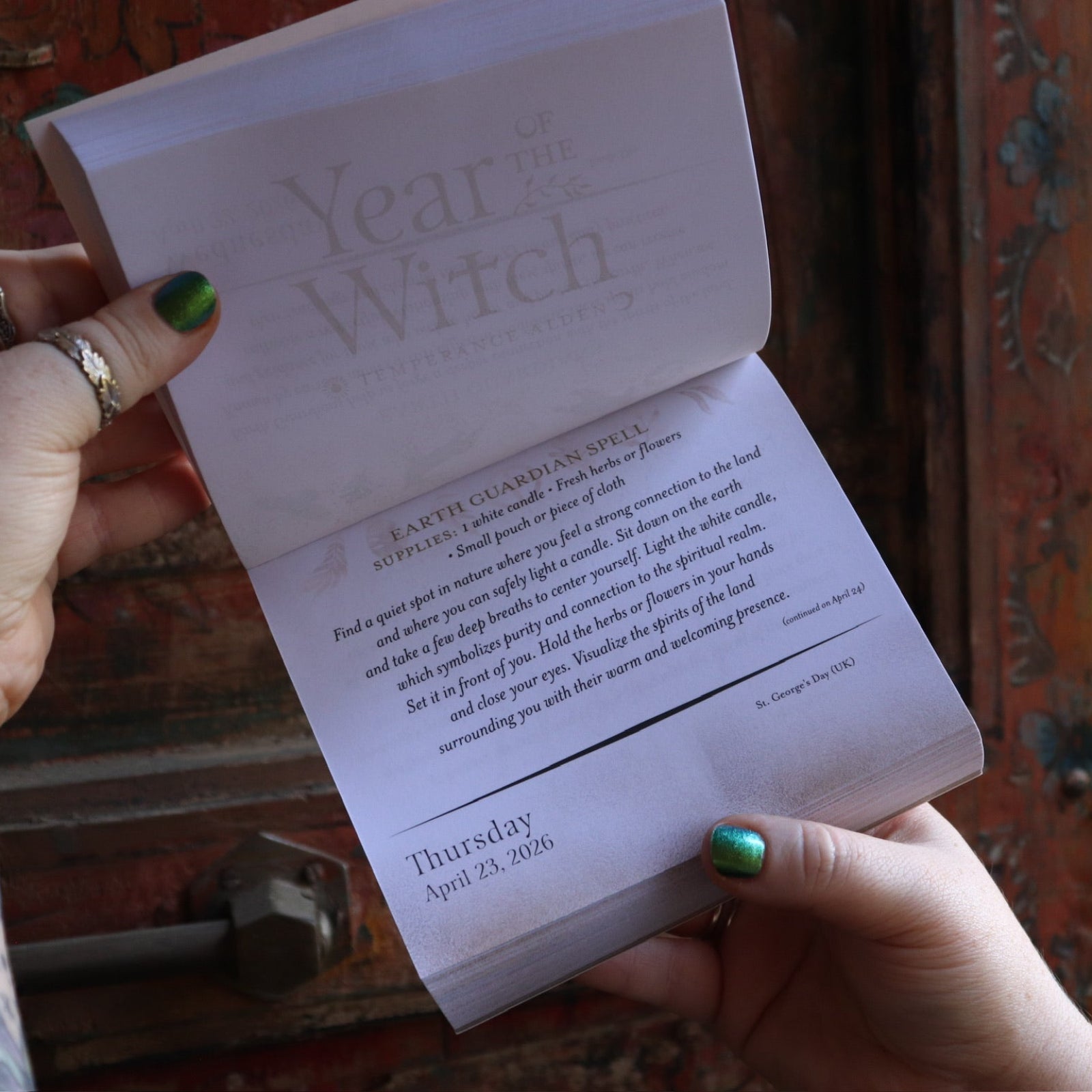 Someone holding the Year of the Witch 2026 Day-to-Day Calendar up in front of a door, showing off the pages.