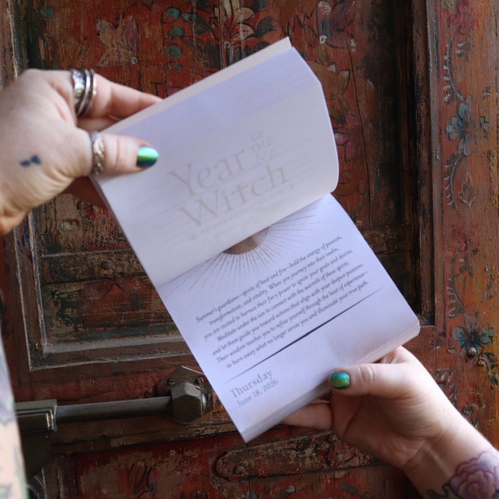 Someone holding the Year of the Witch 2026 Day-to-Day Calendar up in front of a door, showing off the pages.