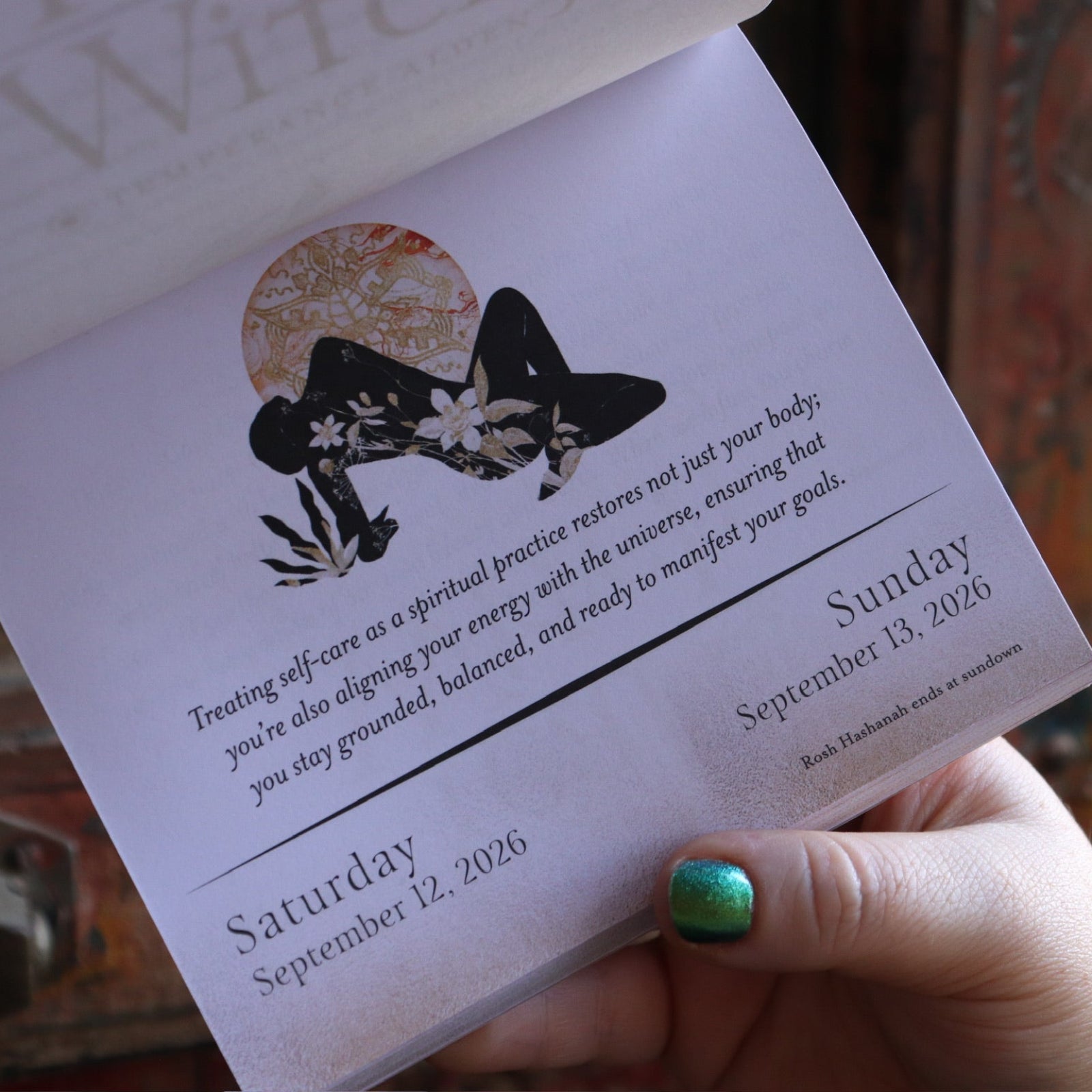 Someone holding the Year of the Witch 2026 Day-to-Day Calendar up in front of a door, showing off the pages.