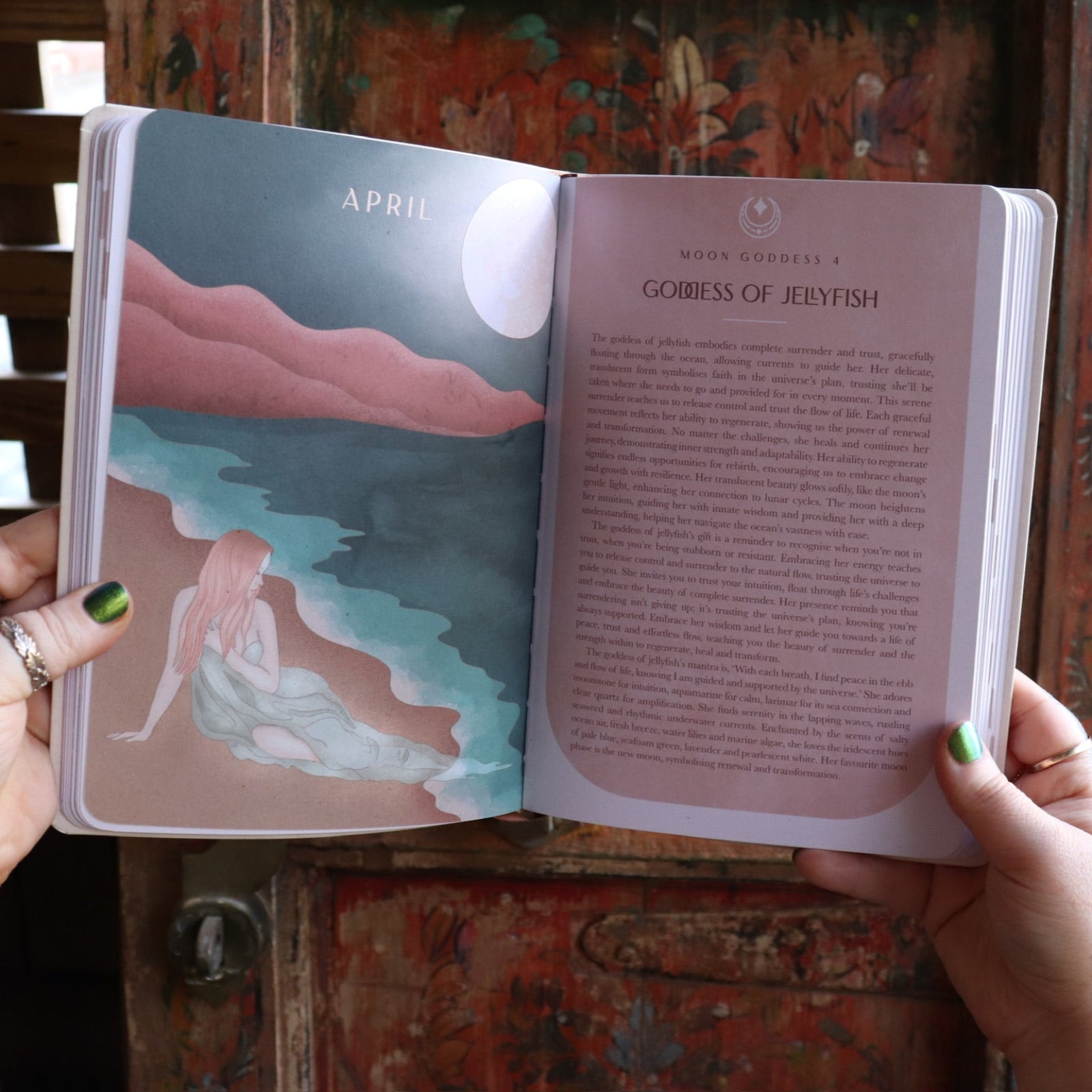 Someone holding the 2026 Moon Goddess Northern Hemisphere Planner Calendar in front of a wooden door, showing off the pages.