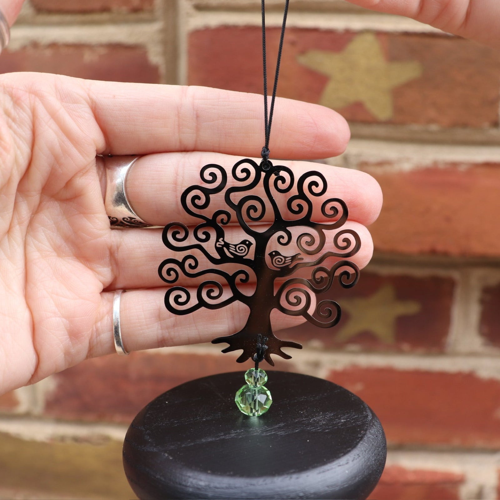 An up-close image of someone holding up the Crystal Tree of Life Wind Chime in front of a brick wall.