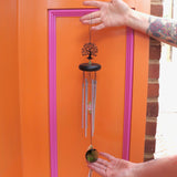 Someone holding up the Crystal Tree of Life Wind Chime in front of an orange and pink wall.