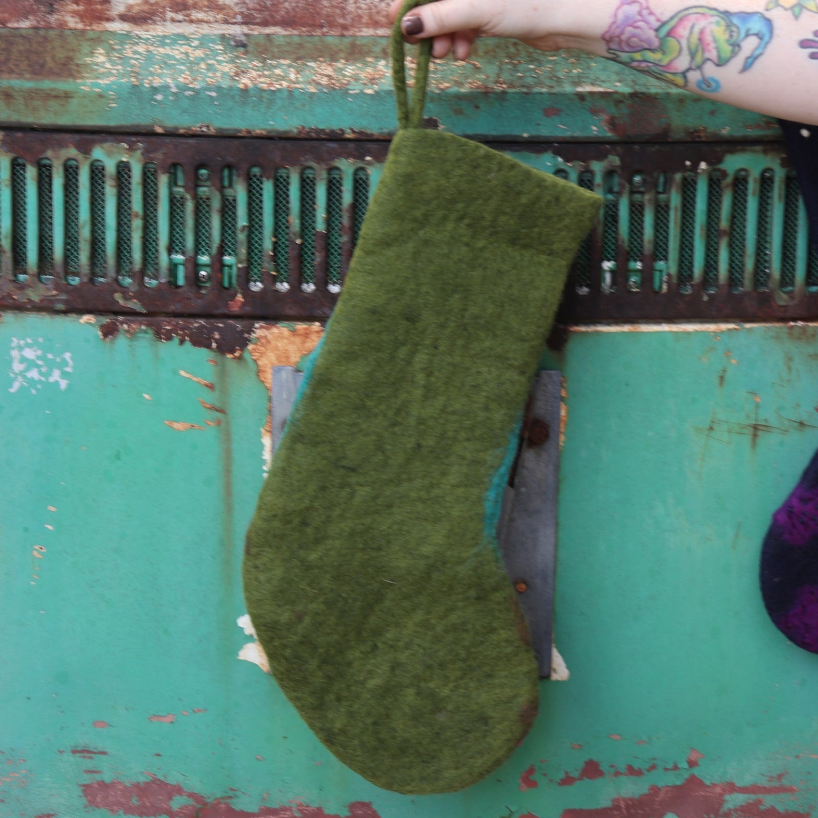 Someone holding the butterfly Folk Art Embroidered Pure Wool Felt Handcrafted Stocking in front of a vintage teal Volkswagen bus, showing off the back.