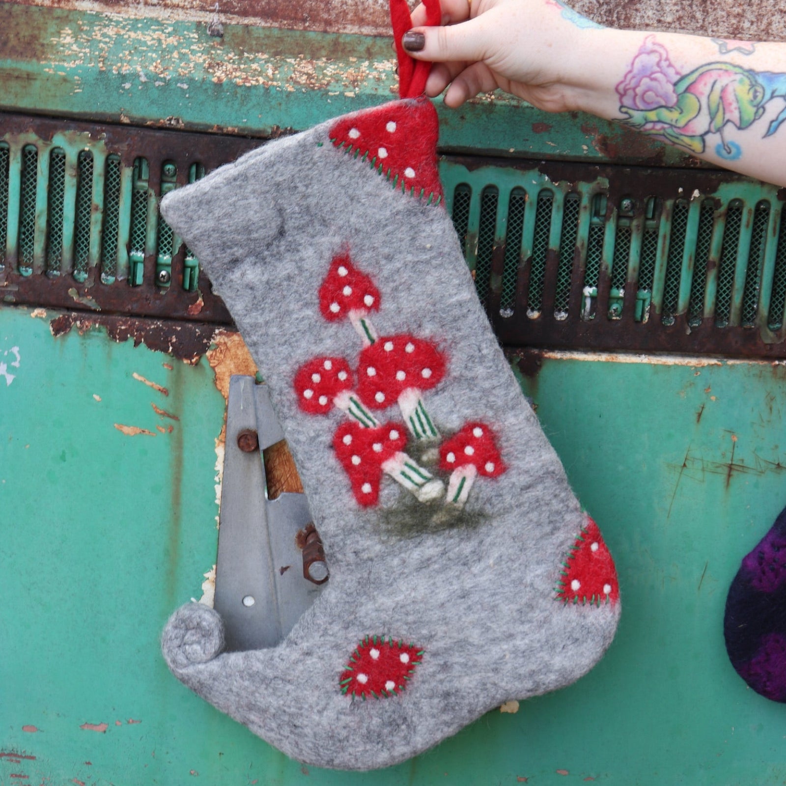 Someone holding the Handmade Red Mushroom Wool Felt Boho Stocking in front of a vintage teal Volkswagen bus.