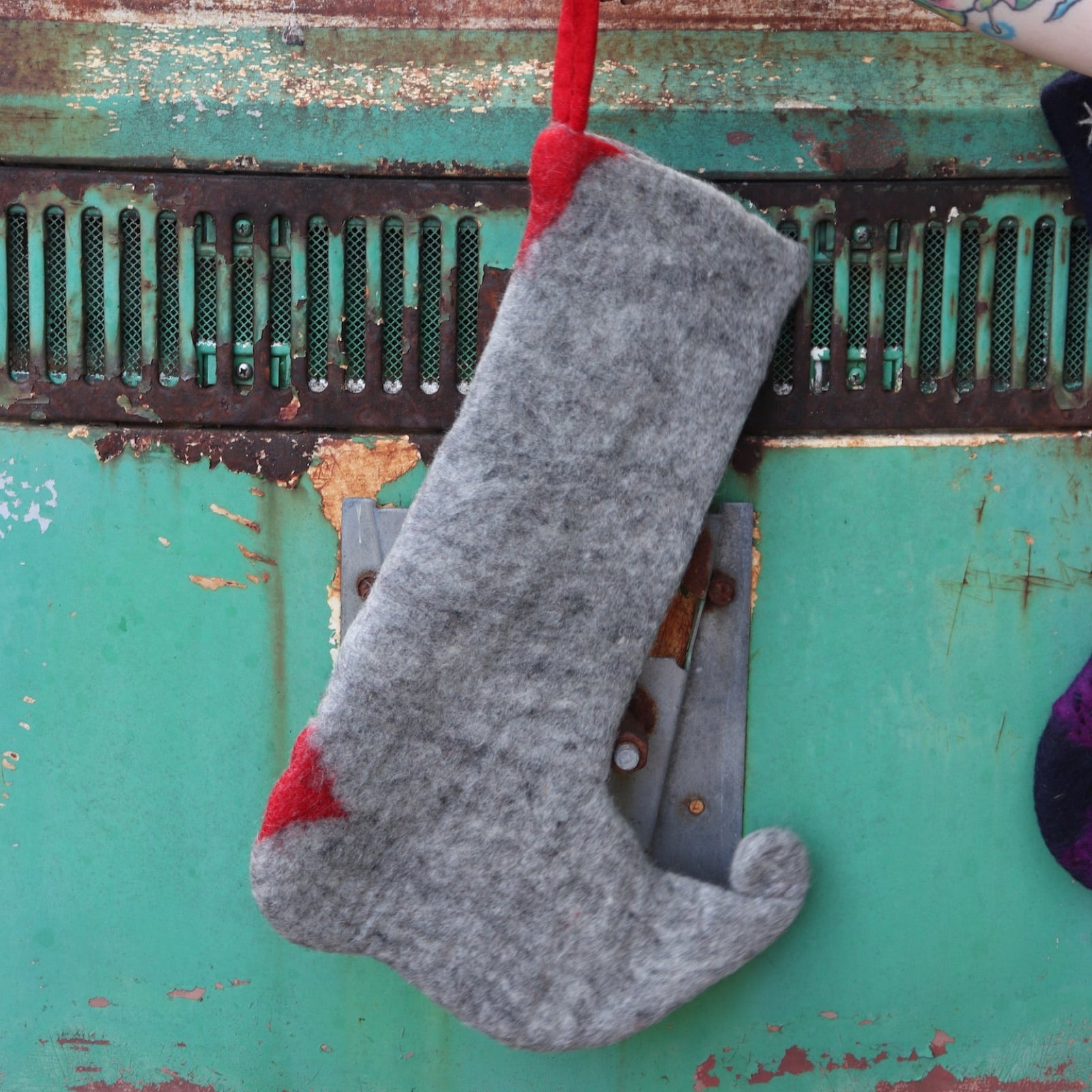 Someone holding the Handmade Red Mushroom Wool Felt Boho Stocking in front of a vintage teal Volkswagen bus, showing off the back.