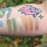 Someone wearing test swabs on their arm of the Plant Medicine 6 Pan Vegan Eyeshadow Palette in front of a green bush.