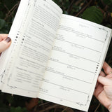 Someone holding The Practical Witch's 2026 Almanac open in front of some greenery.