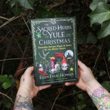 Someone holding the Sacred Herbs of Yule and Christmas in front of a green bush.