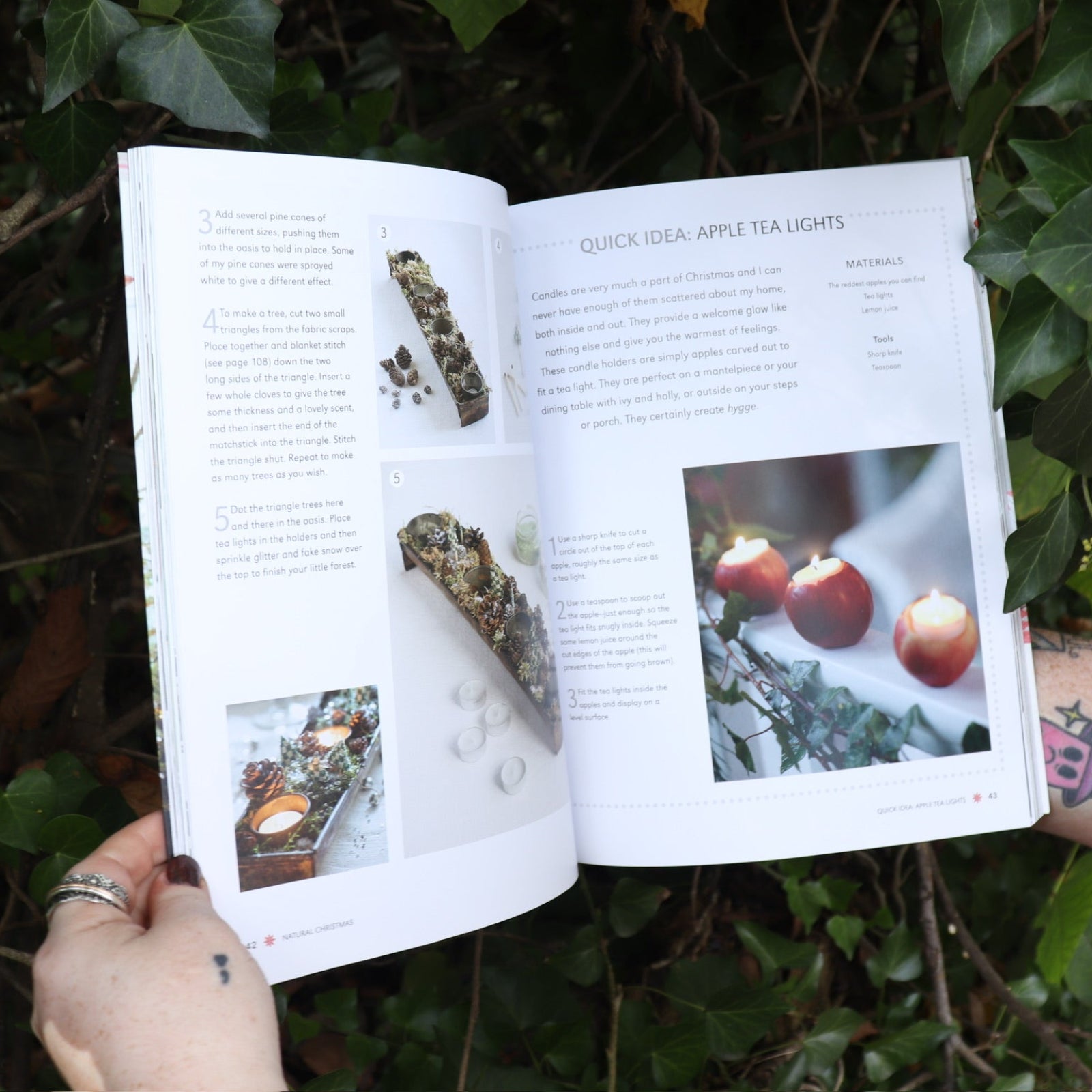 Someone holding the Scandinavian Christmas Crafts Paperback Book open in front of a green bush, showing off the pages.