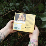 Someone holding the Punk History 2026 Day-to-Day Calendar in front of a green bush, showing off the back.