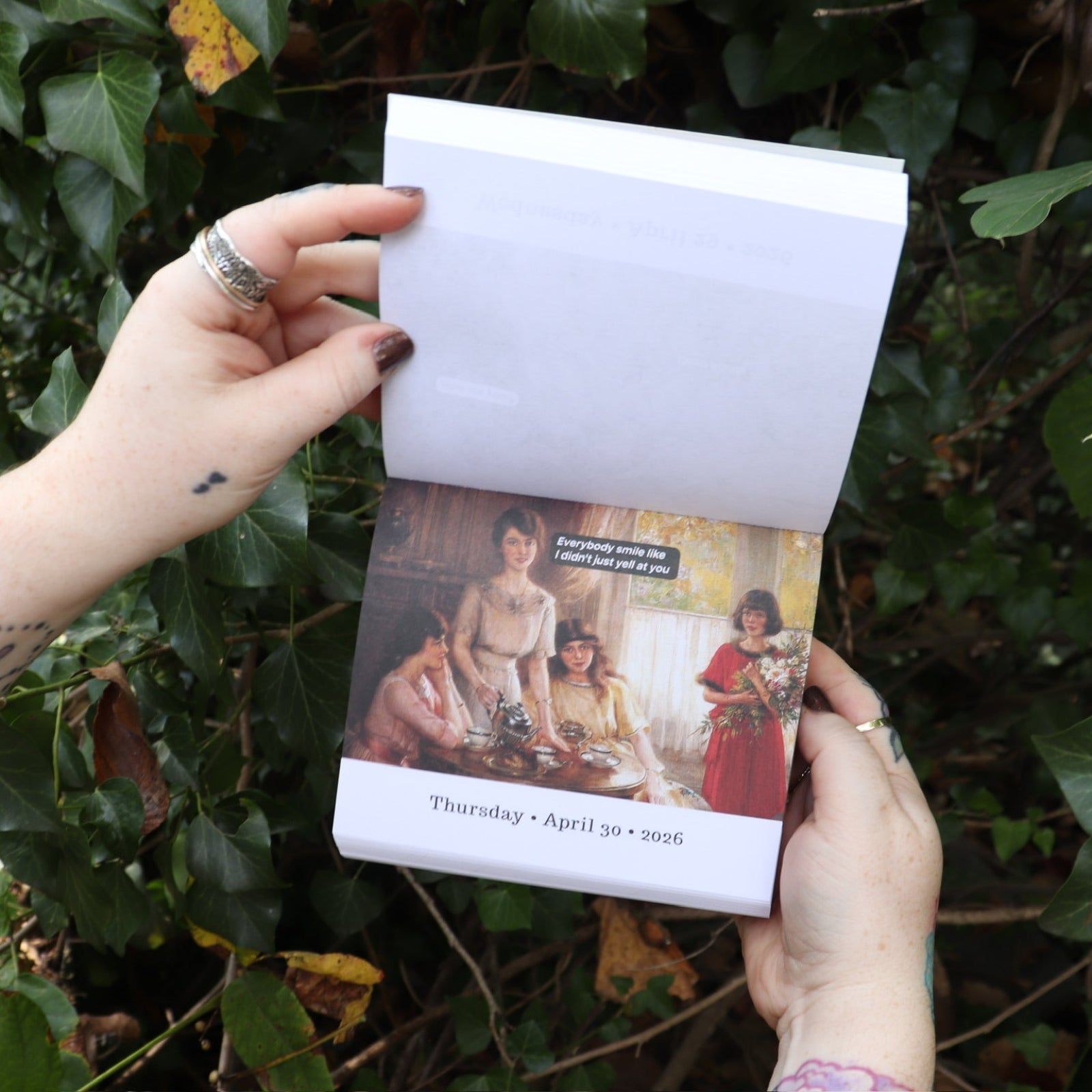 Someone holding the Punk History 2026 Day-to-Day Calendar open in front of a green bush, showing off the pages.
