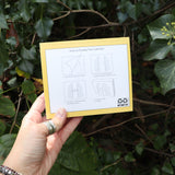 Someone holding the Punk History 2026 Day-to-Day Calendar in front of a green bush.