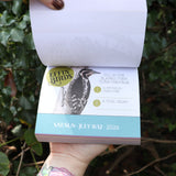 Someone holding the Effin' Birds 2026 Day-to-Day Calendar open in front of a green bush, showing off the pages.