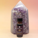 The Prosperity Reiki Charged Anointing Oil in front of an amethyst tower all on a pink and yellow background.