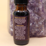 The Prosperity Reiki Charged Anointing Oil in front of an amethyst tower all on a pink and yellow background.