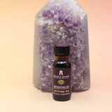 The Letting Go Reiki Charged Anointing Oil in front of an amethyst tower all on a pink and yellow background.