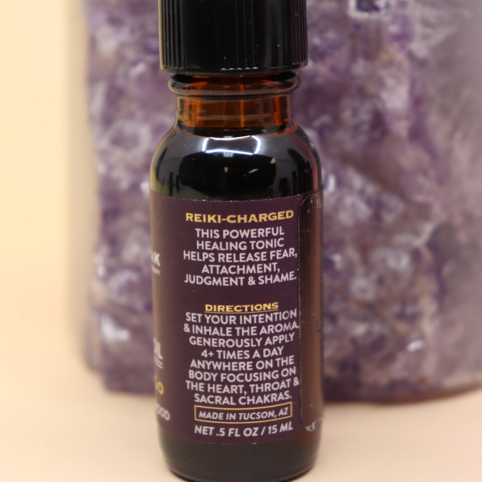 The Letting Go Reiki Charged Anointing Oil in front of an amethyst tower all on a pink and yellow background.