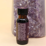 The Fearlesssness & Confidence Reiki Charged Anointing Oil in front of an amethyst tower all on a pink and yellow background.