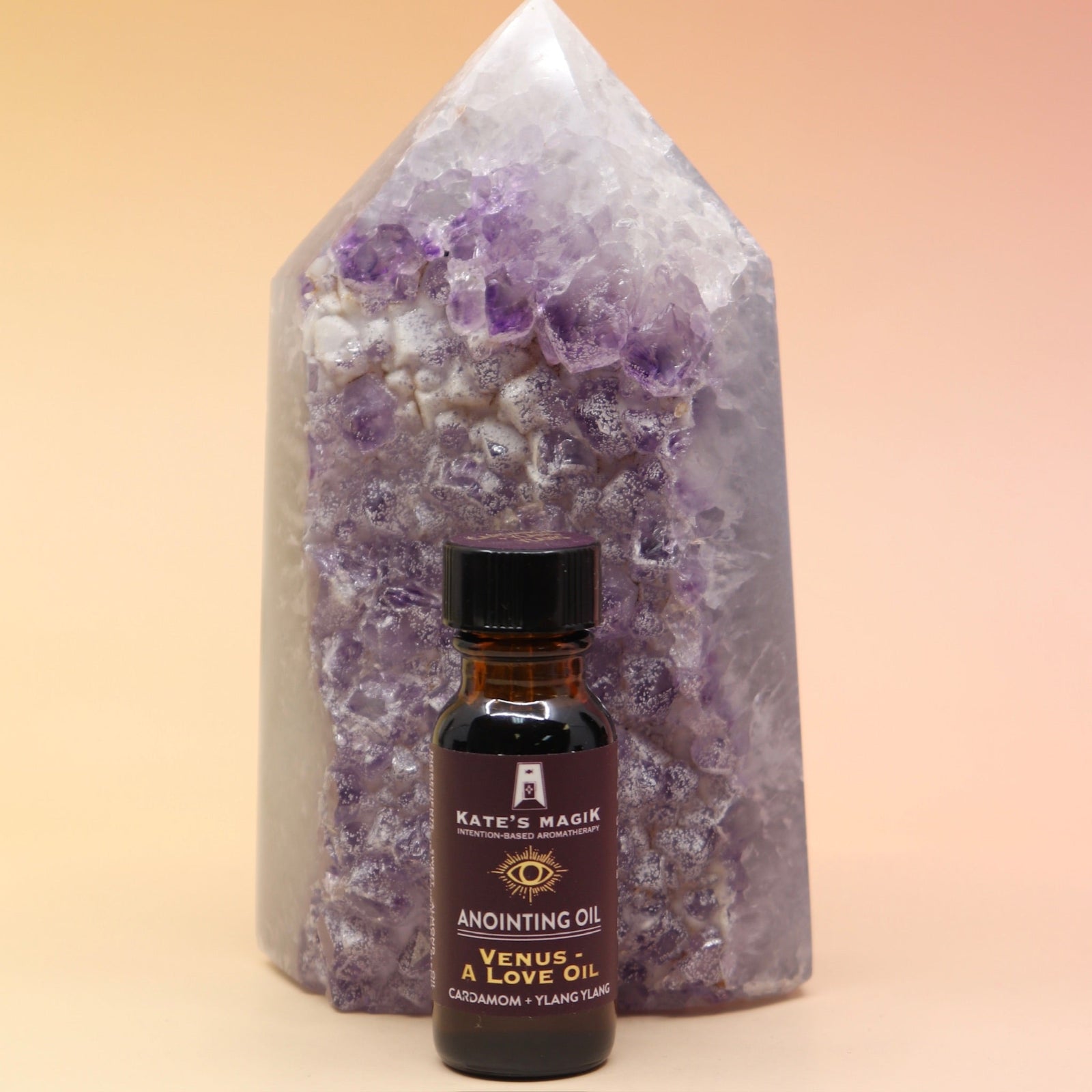 The Venus - A Love Oil Reiki Charged Anointing Oil in front of an amethyst tower all on a pink and yellow background.