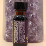 The Break Patterns & Addictions Oil Reiki Charged Anointing Oil in front of an amethyst tower all on a pink and yellow background.