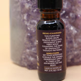 The Uncrossing Oil Reiki Charged Anointing Oil in front of an amethyst tower all on a pink and yellow background.