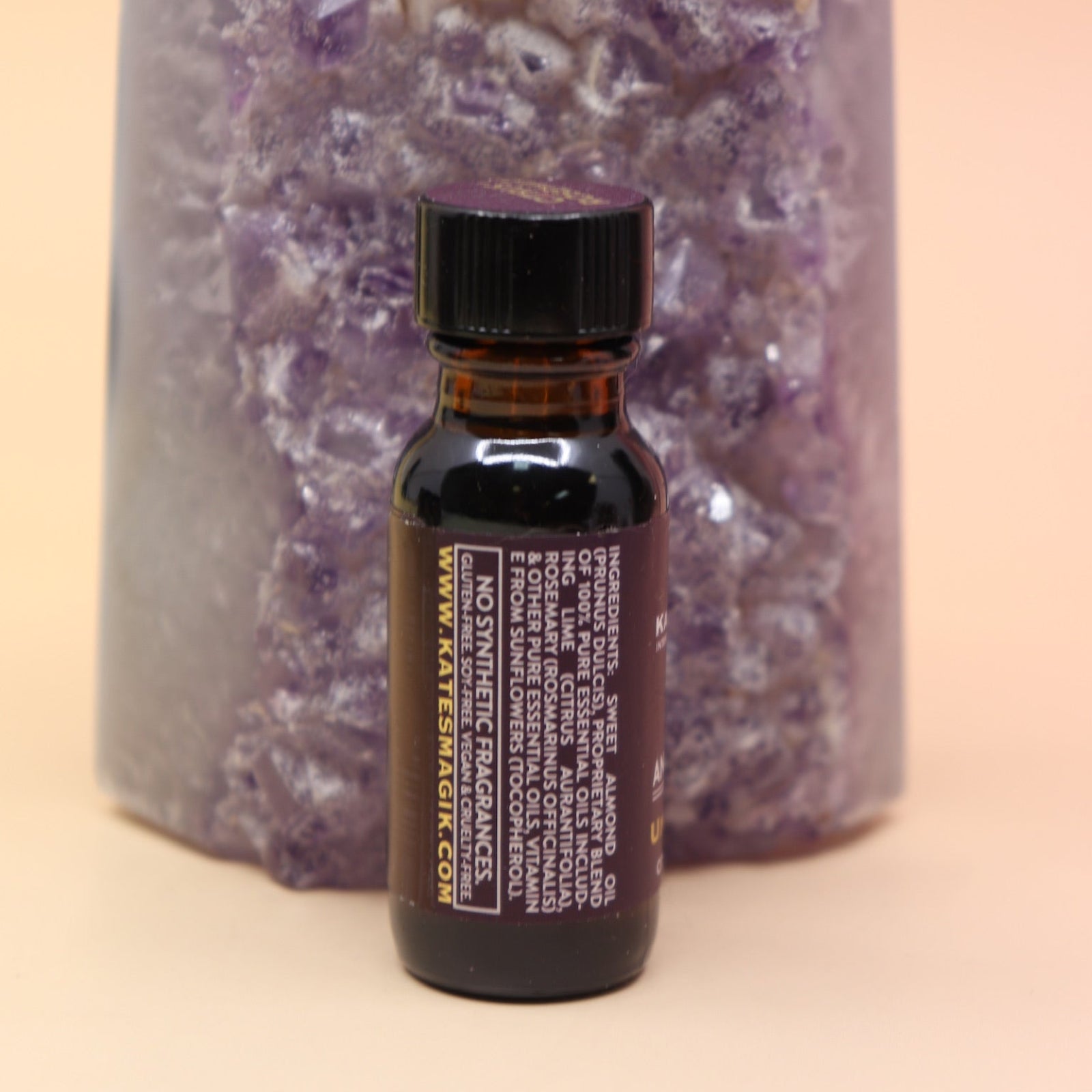 The Uncrossing Oil Reiki Charged Anointing Oil in front of an amethyst tower all on a pink and yellow background.