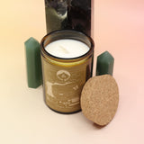 The Golden Days 12oz Soy Candle in front of a large crystal tower surrounded by two smaller crystal towers all on a pink and yellow background.