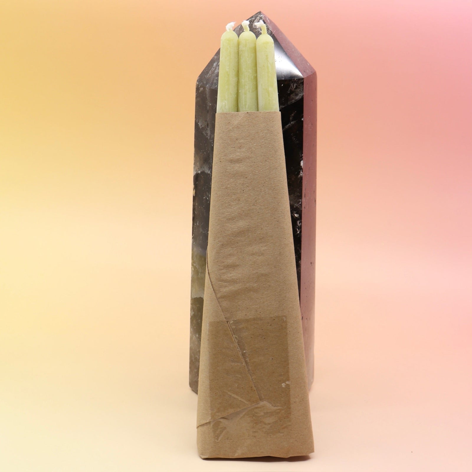 The straight Chartreuse Beeswax Taper Candles against a crystal tower all on a pink and yellow background, showing off the back.