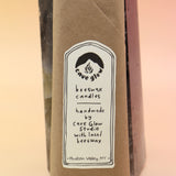 An up-close image of the packaging of the Cave Glow Studio Taper Candles against a crystal tower all on a pink and yellow background.