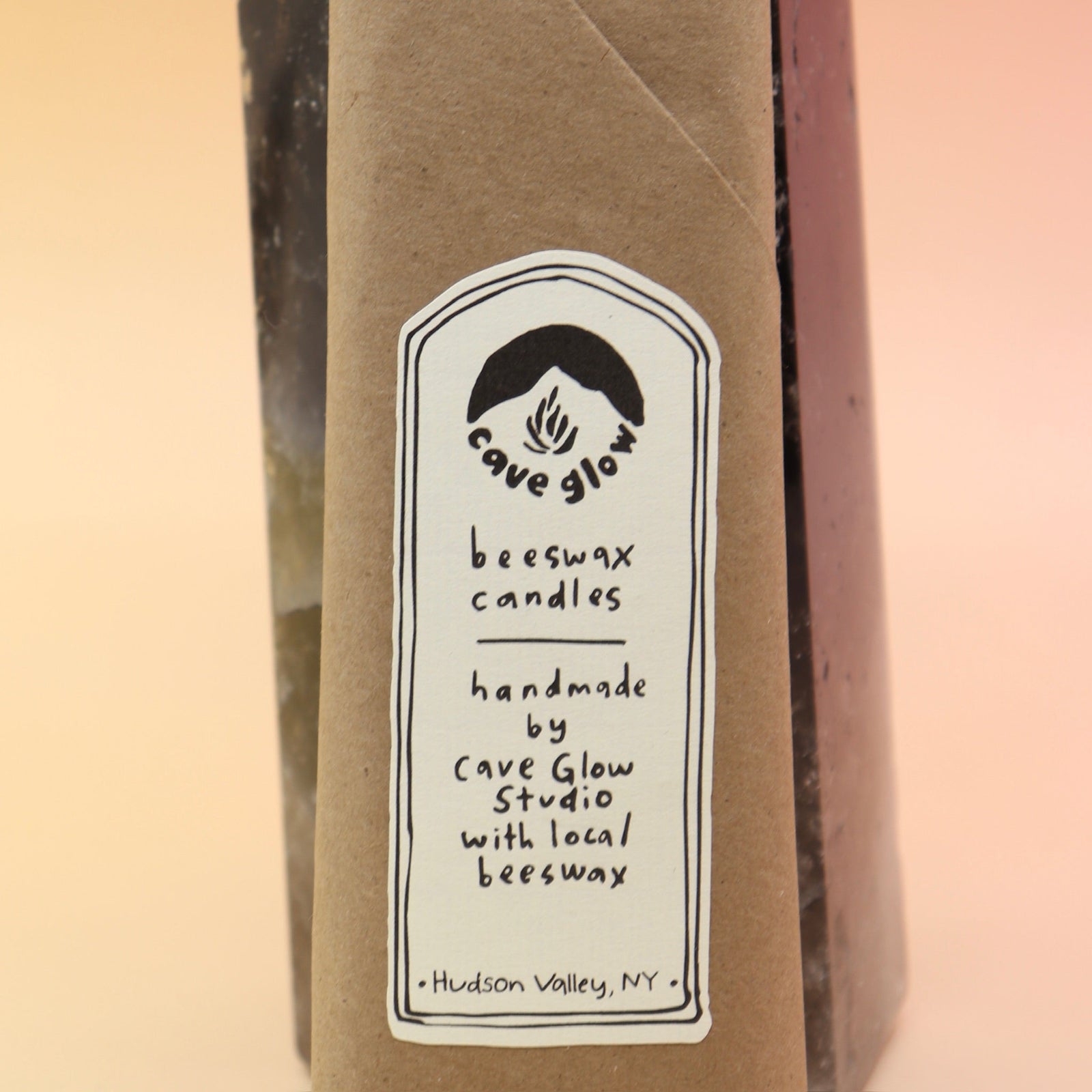 An up-close image of the packaging of the Cave Glow Studio Taper Candles against a crystal tower all on a pink and yellow background.