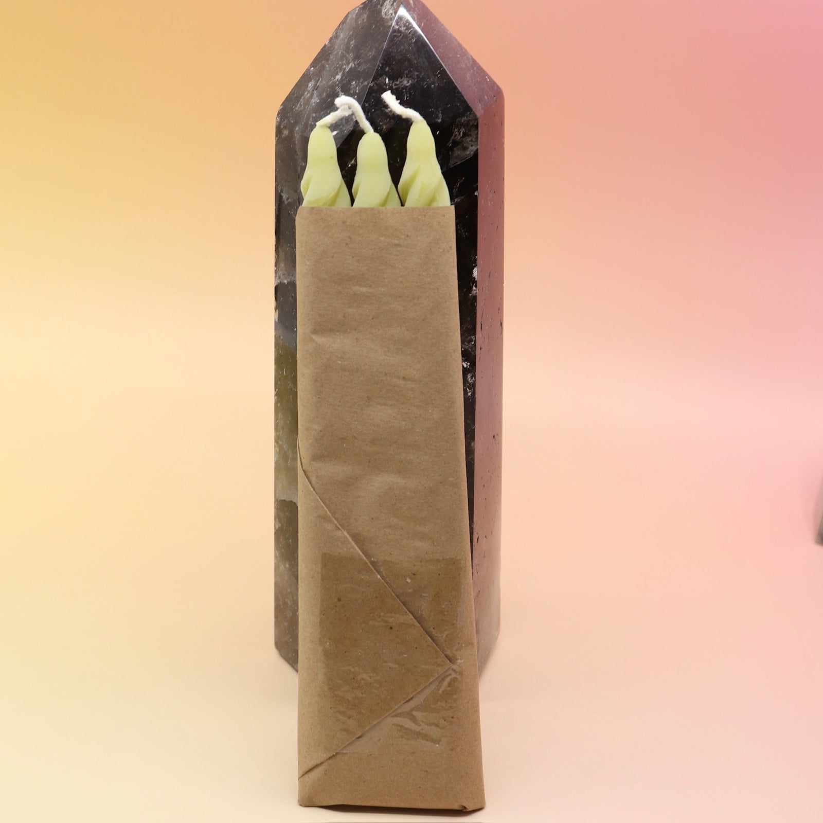 The spiral Chartreuse Beeswax Taper Candles against a crystal tower all on a pink and yellow background, showing off the back.