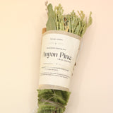 The Piñon Pine Sacred Smoke Cleansing Stick with Quartz Crystal on a pink and yellow background.
