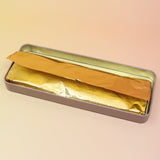 The Soft Sunset Premium Incense on a pink and yellow background, showing off the inside of the tin.