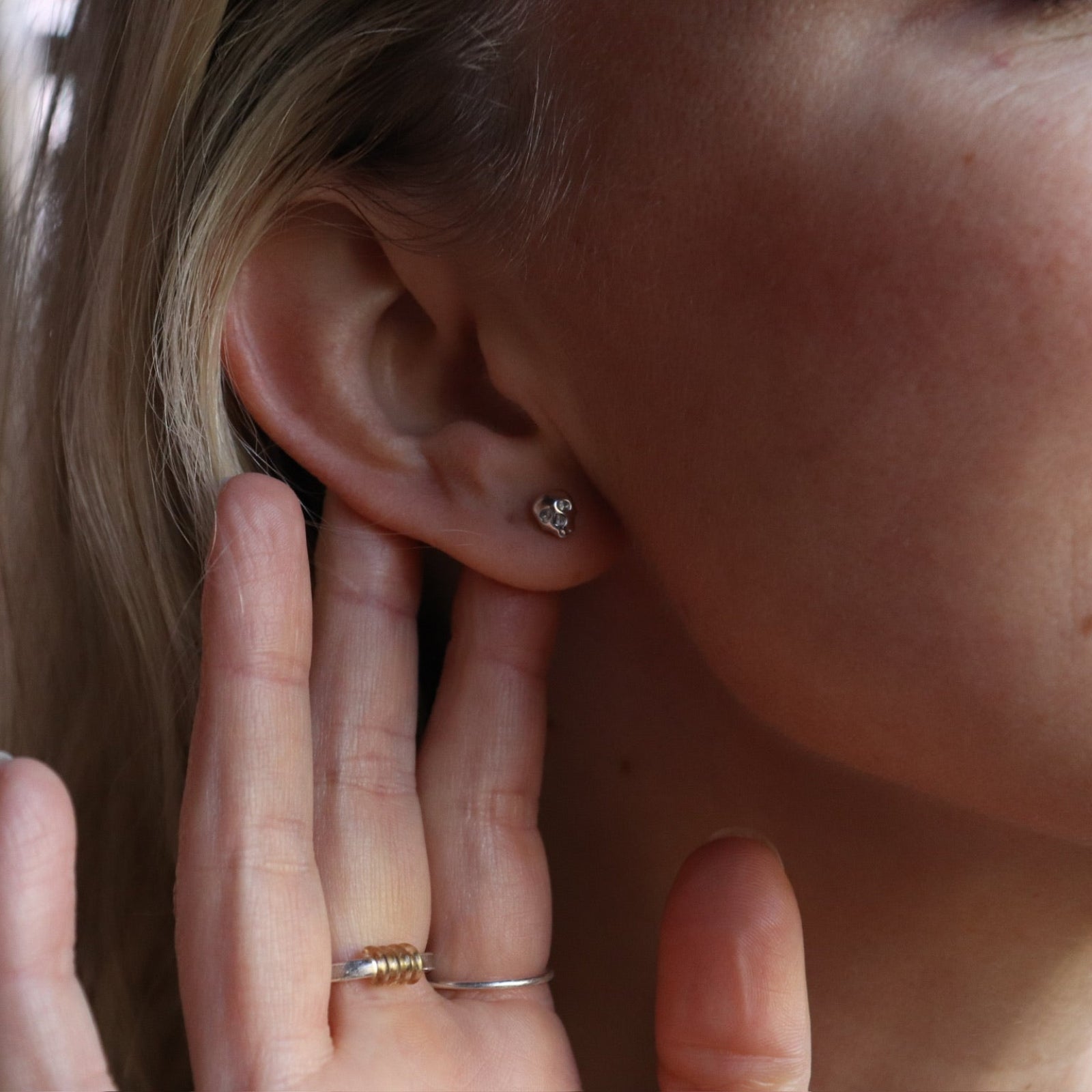 An up-close image of someone wearing the silver Memento Mori Mini Skull Stud Earrings.
