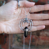 Someone holding the Silver Thorn Crystal Necklace in front of a wooden background.