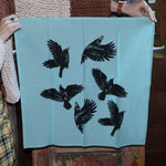 Someone holding up the Crows Cotton Bandana in front of a wooden background.