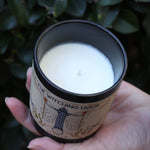 Someone holding the Witching Hour Garden Candle in front of a green bush, showing off the inside.