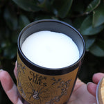 Someone holding the Clear the Vibes Soy Wax Garden Energy Clearing Candle in front of a green bush, showing off the inside.