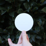 Someone holding the Actual Ghost Holographic Sticker in front of a green bush, showing off the back.