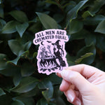 Someone holding the Feminist Halloween Sticker in front of a green bush.