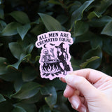 Someone holding the Feminist Halloween Sticker in front of a green bush.