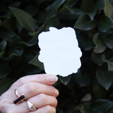 Someone holding the Vintage Halloween Sticker in front of a green bush, showing off the back.
