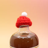 The red Mini Knit Cap on top of a bottle on a pink and yellow background.