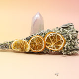 The Citrus Harvest Fall & Winter Sage Bundle in front of a crystal tower all on a pink and yellow background.