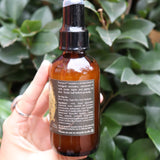 Someone holding the Krampus Scented Veil Spray in front of a green bush.