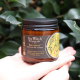 Someone holding the Krampus Soy Wax 3 oz Candle in front of a green bush.