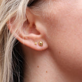 Someone wearing the gold Memento Mori Mini Skull Stud Earrings.